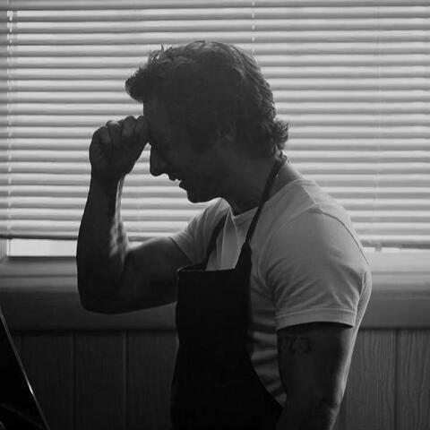 a black and white photo of carmy berzatto from the bear looking left.