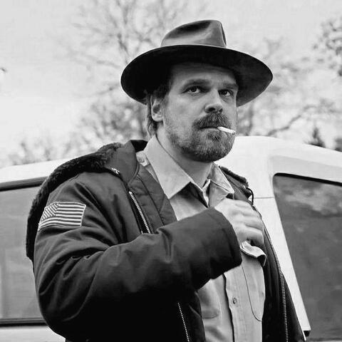 a black and white photo of jim hopper from stranger things looking right.